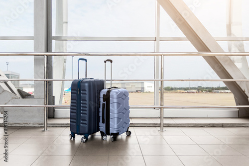 Two Stylish Plastic Luggage Suitcases Standing Near Panoramic Window At Airport, Blue And Beige Travel Bags Waiting In Terminal, Creative Shot For Transportration And Travelling Concept, Copy Space photo