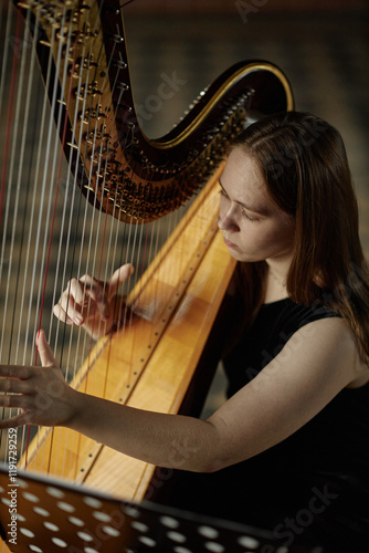 Foto Vertical portrait shot of of graceful young woman playing harp softly looking do
