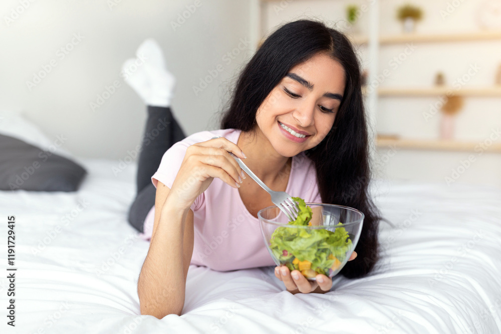 Slimming diet concept. Lovely Indian lady eating tasty vegetable salad on comfy bed at home. Attractive Hindu woman leading healthy lifestyle, losing weight, taking care of her body, indoors Slimming diet concept. Lovely Indian lady eating tasty vegetable salad on comfy bed at home. Attractive Hindu woman leading healthy lifestyle, losing weight, taking care of her body, indoors