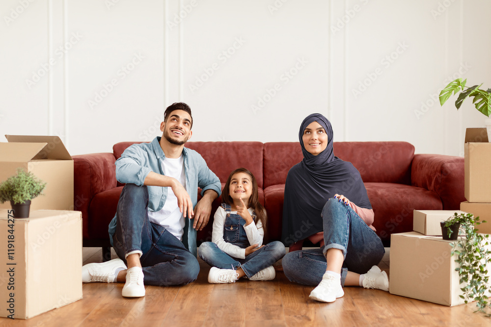 Portrait of smiling muslim family sitting on the floor among boxes leaning on sofa in new apartment, doing repair. Little daughter pointing finger up, people choosing wall color and interior design Portrait of smiling muslim family sitting on the floor among boxes leaning on sofa in new apartment, doing repair. Little daughter pointing finger up, people choosing wall color and interior design