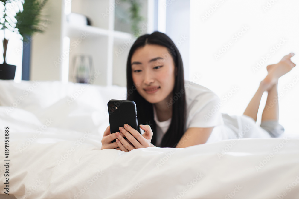 Asian woman in twenties lying on bed using smartphone. Relaxed atmosphere, connected with digital world, enjoying leisure time. Bright room, peaceful setting, modern lifestyle conveyed. Asian woman in twenties lying on bed using smartphone. Relaxed atmosphere, connected with digital world, enjoying leisure time. Bright room, peaceful setting, modern lifestyle conveyed.