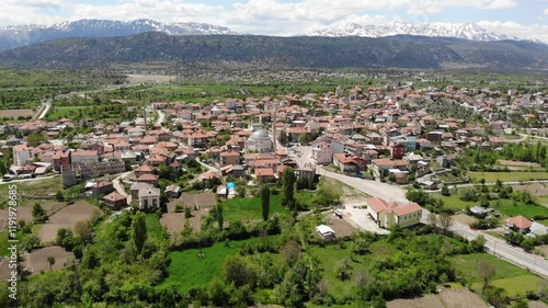 Scenic spring view from drone of Yesildag village with residential houses and mosque in green valley surrounded by mountains with peaks covered with snow, Turkey photo