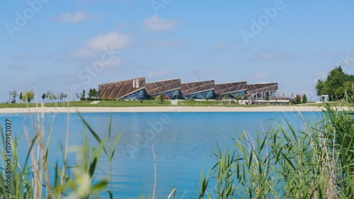 The modern Expano building in Murska Sobota, Slovenia, surrounded by a calm lake on a bright summer day. The video captures the architecture, clear sky, and serene waters reflecting the scenery. photo