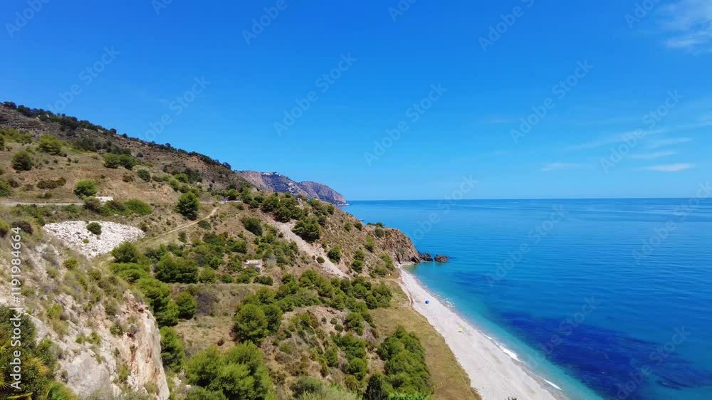 The beautiful white sand beach and crystal clear water from the hillside in southern Spain. There are colorful sun umbrellas on the beach. A small road leads along the nature on the mountainside. The beautiful white sand beach and crystal clear water from the hillside in southern Spain. There are colorful sun umbrellas on the beach. A small road leads along the nature on the mountainside.