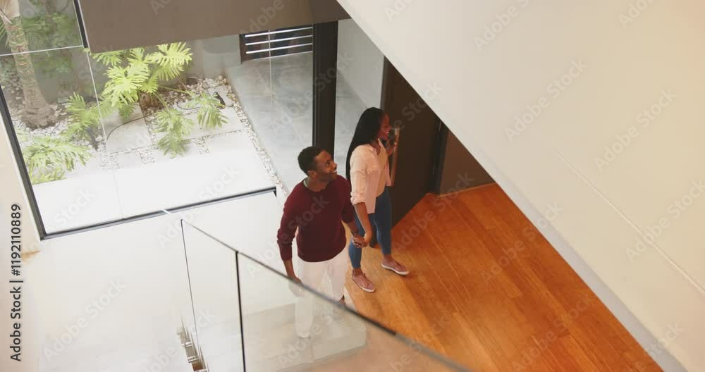 Smiling african american man walking up stairs while african american woman stands in home entryway Smiling african american man walking up stairs while african american woman stands in home entryway