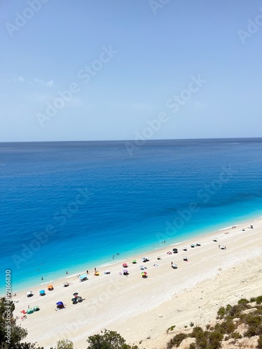 Egremni beach, Lefkada, Greece. Rich, deep blue, crystal clear water and pure white sand with colourful beach umbrellas and people swimming. 