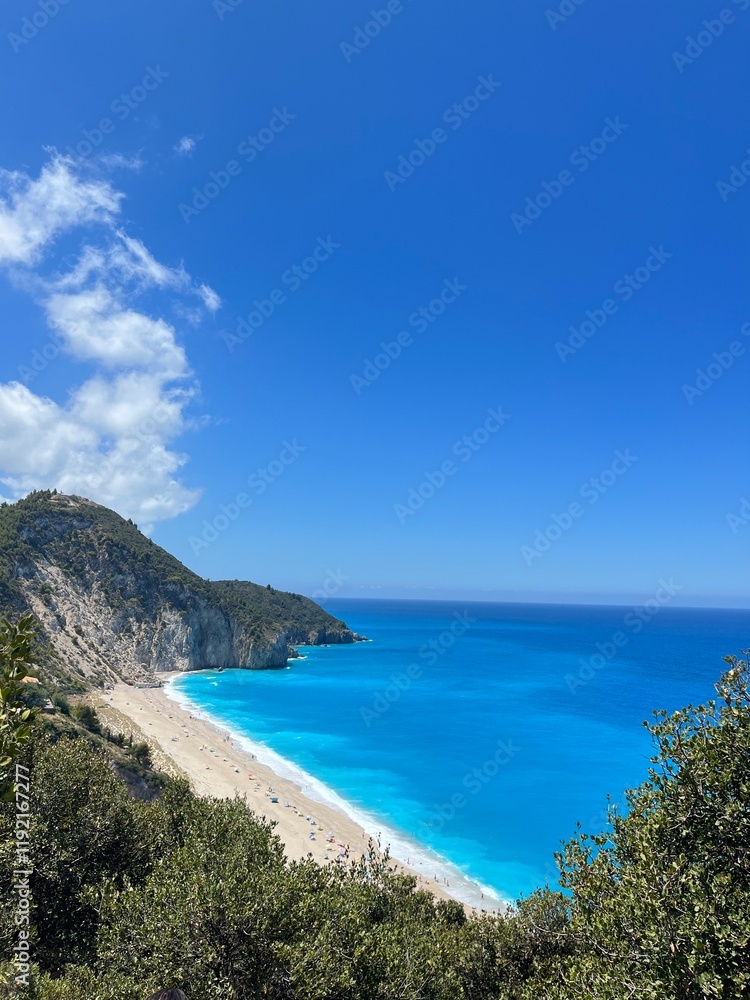 Milos beach, Lefkada, Greece landscape. Image taken from the mountain above. Featuring rich blue water, clear skies, people on the beach and shrubs in the mountain. Unreal beach and heavenly. water. Milos beach, Lefkada, Greece landscape. Image taken from the mountain above. Featuring rich blue water, clear skies, people on the beach and shrubs in the mountain. Unreal beach and heavenly. water.