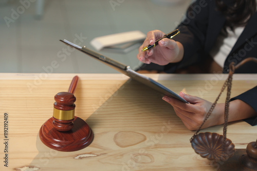 Female lawyer reviewing legal documents, pointing with a pen, with a gavel and scales of justice on the table, symbolizing law, justice, and legal proceedings photo