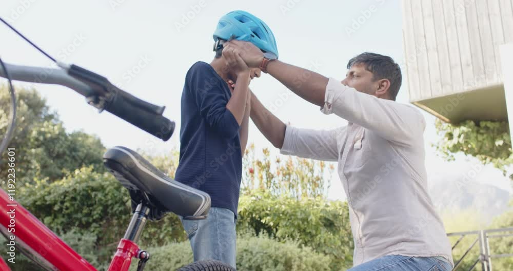 Indian father helping young son adjust helmet while preparing to ride bicycle Indian father helping young son adjust helmet while preparing to ride bicycle