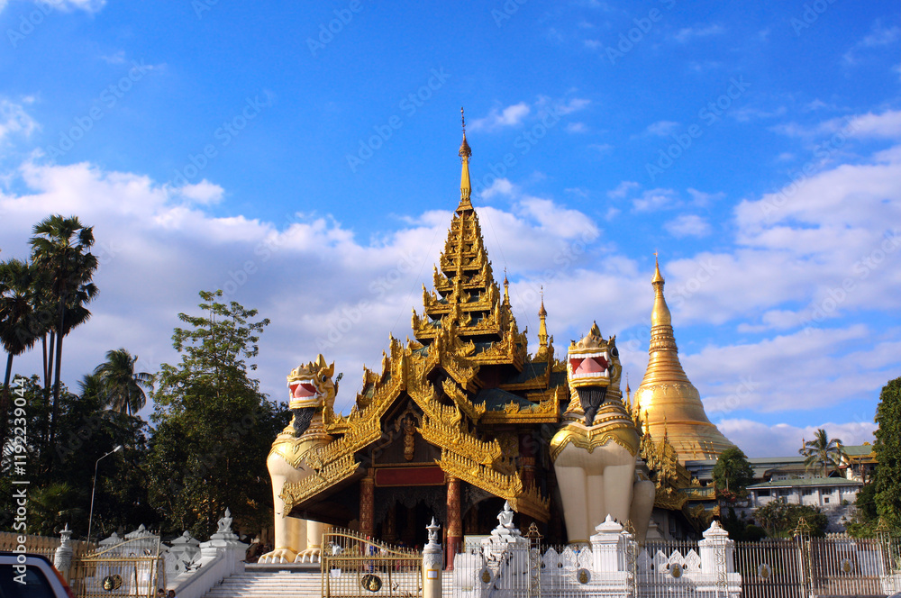 Fototapeta premium Golden statue of lion guardian and golden stupa in ancient buddhist complex. Stone figures of mythical creatures near to buddhist temple, Yangon, Myanmar (Burma)