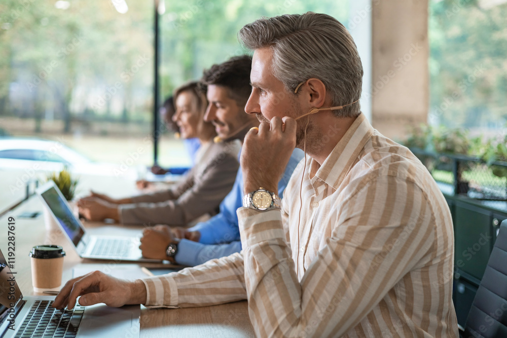 Fototapeta premium Portrait of call center worker accompanied by his team. Smiling customer support operator at work.