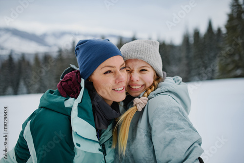 Mom and cute girl hugging, standing in the middle of snowy nature. photo