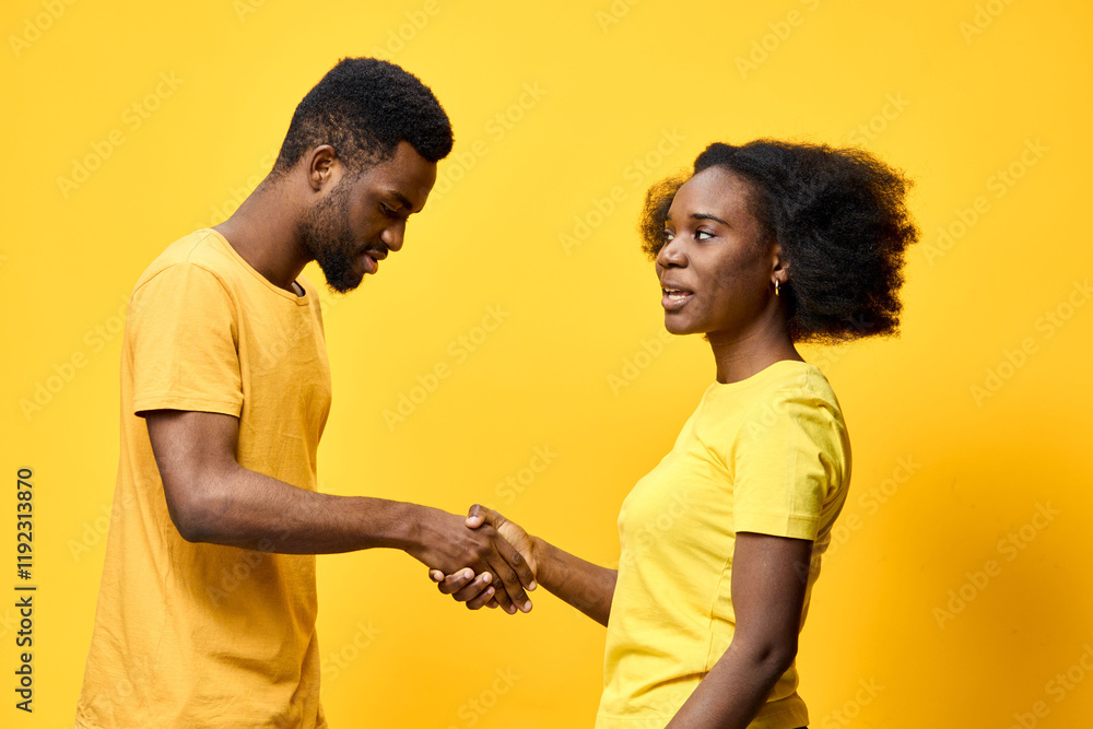 Obraz premium Young African couple shaking hands in matching yellow attire against a vibrant yellow background, symbolizing unity and collaboration in friendship or business