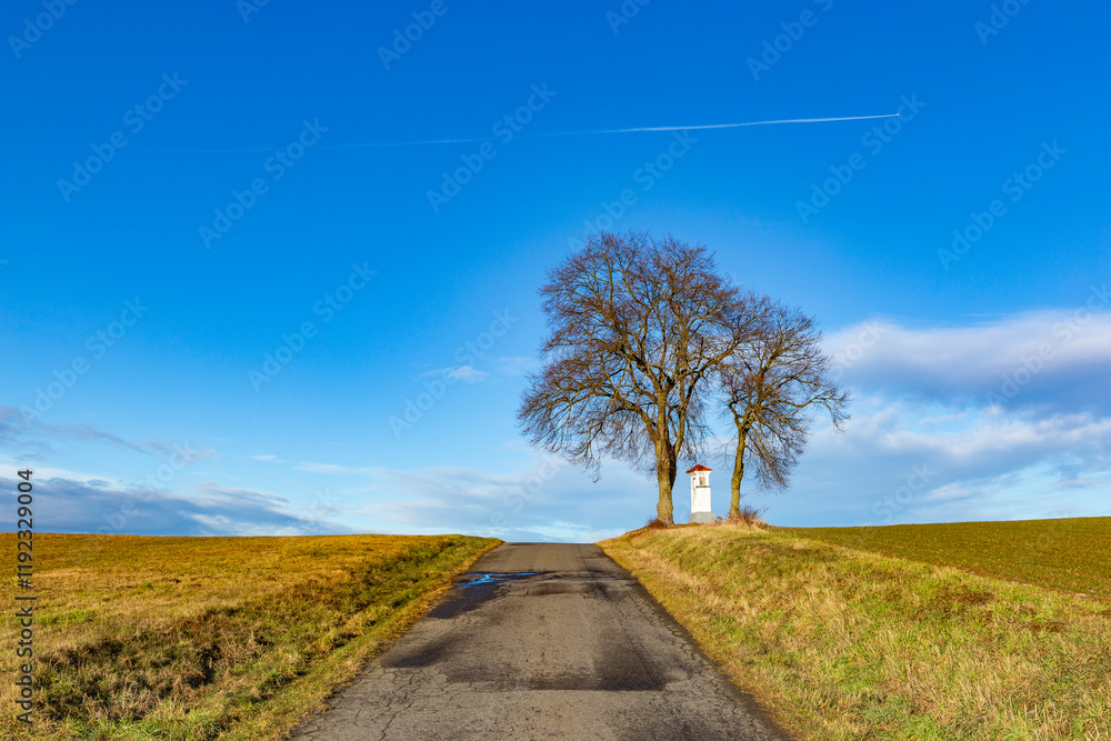 A small chapel on top of a hill with two trees above it. Czechia.