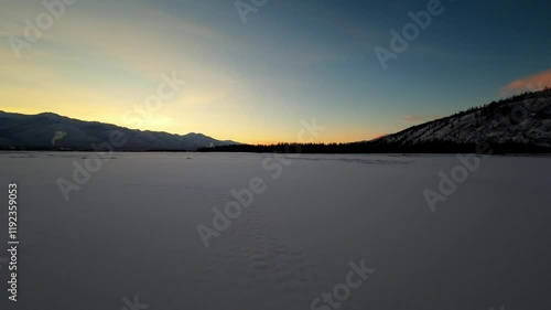 Wallpaper Mural A captivating sunset unfolds over a vast frozen lake, with majestic mountains and dense woods framing the tranquil winter scene. The sky transitions into warm hues as night approaches. Torontodigital.ca