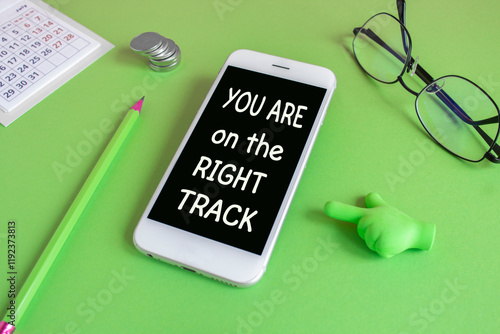 Motivational quoter You are on The Right Track. Concept words You are on The Right Track written on the mobile phone screen. Beautiful green background. Glasses, coins. Business concept. photo