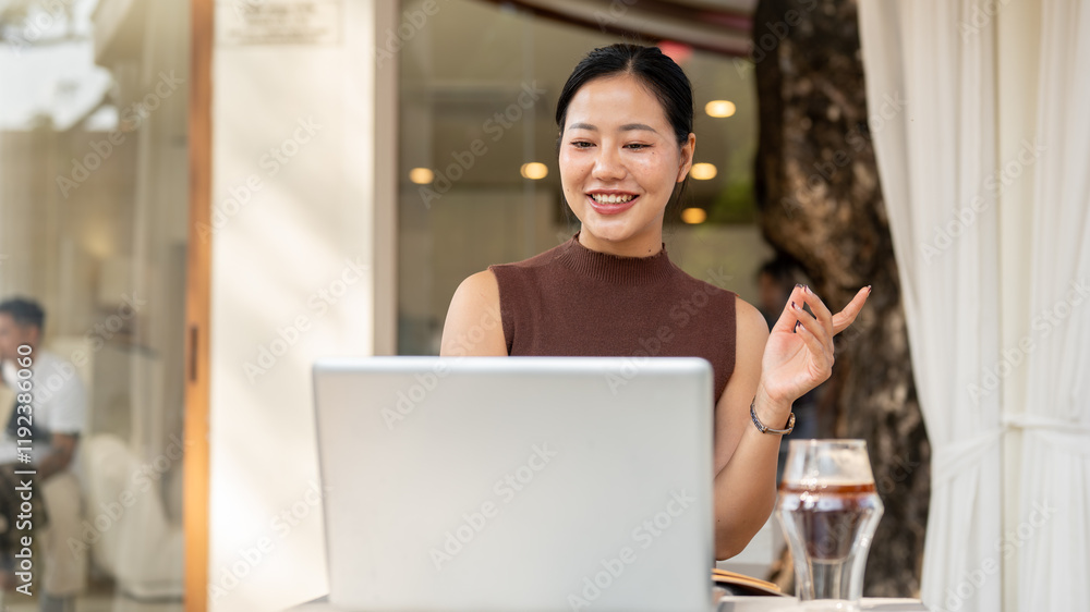 A happy, confident Asian woman is working remotely from a cafe, participating in an online meeting. A happy, confident Asian woman is working remotely from a cafe, participating in an online meeting.