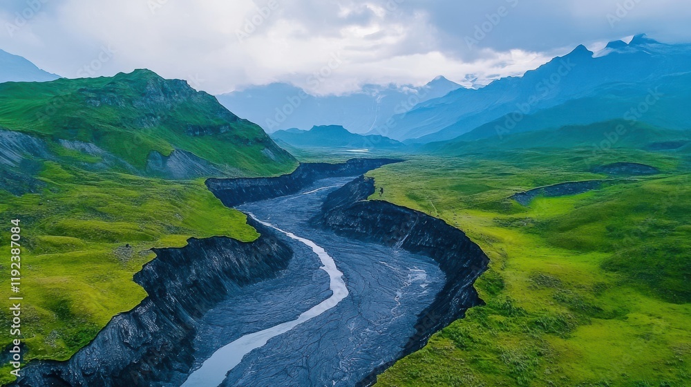 Fototapeta premium Lush green landscapes surround a winding river, framed by majestic mountains under a cloudy sky, showcasing the beauty of nature.