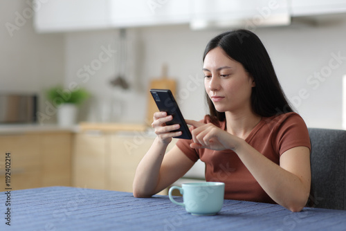 Serious asian woman using smart phone in the kitchen photo