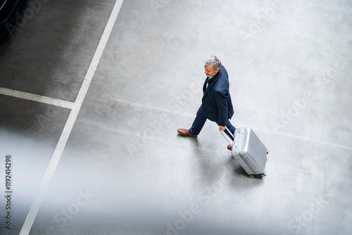 Mature businessman walking with suitcase in parking lot