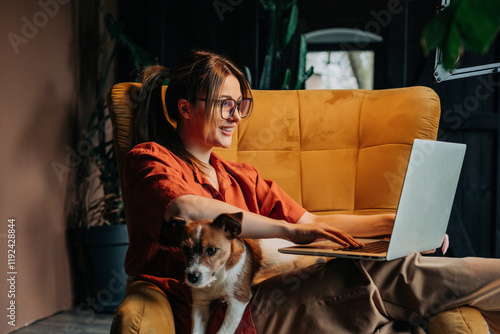 Smiling woman sitting with dog and working on laptop at home photo