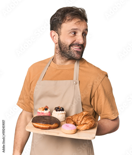 Cuadro en lienzo Hispanic male baker with pastries looks aside smiling, cheerful and pleasant
