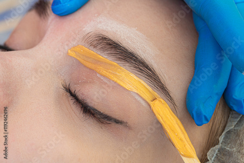 Hands of Professional Beautitian While Completing Eyebrow Correction with Wax and Wooden Sticks in Beauty Salon As Eyebrow Hair Removal with Wax. photo