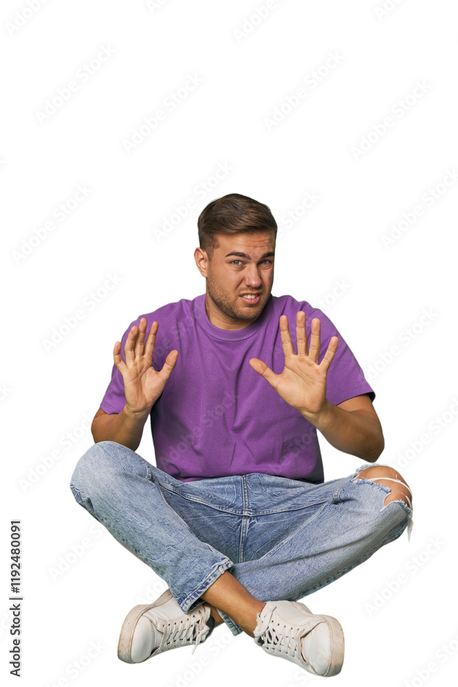 Casual man sitting on floor rejecting someone showing a gesture of disgust. Casual man sitting on floor rejecting someone showing a gesture of disgust.