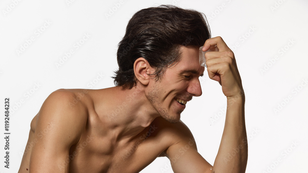 Laughing man applies ice cube on forehead, droplets visible on skin. against white background. Lighthearted, refreshment skincare moment. Concept of male beauty and facial care, cosmetology. Laughing man applies ice cube on forehead, droplets visible on skin. against white background. Lighthearted, refreshment skincare moment. Concept of male beauty and facial care, cosmetology.