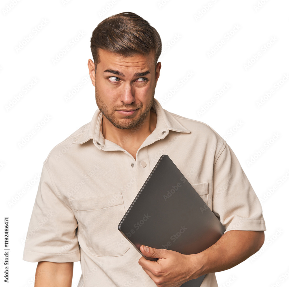 © Asier - Man holding laptop, studio confused, feels doubtful and unsure.