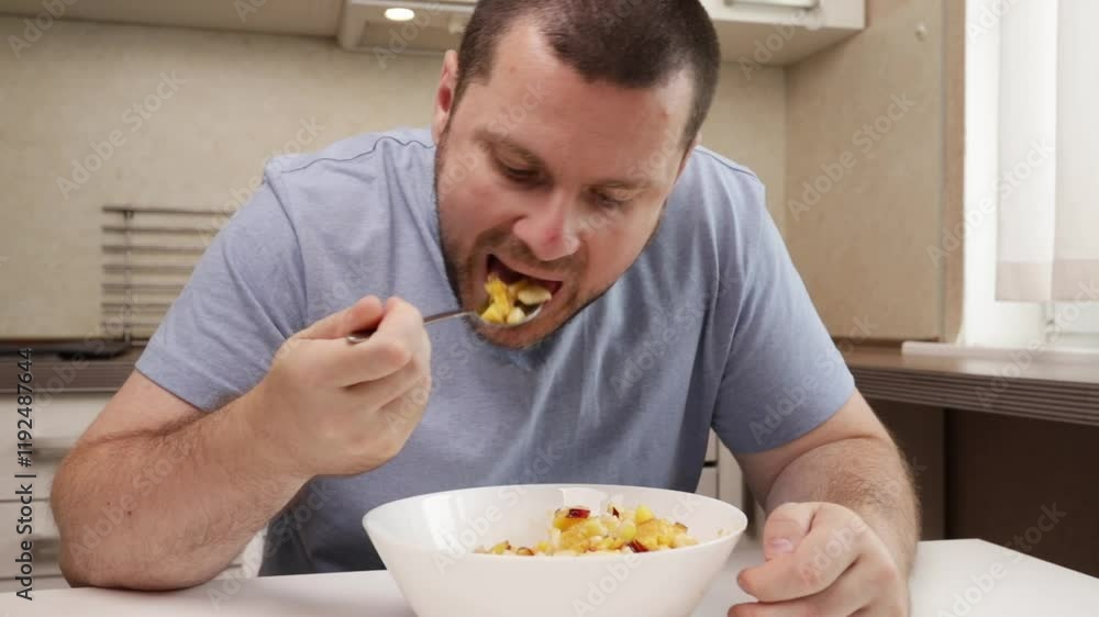 Man Eating Fresh fruit salad, sitting at a modern table in the kitchen, enjoying a homemade meal at home. Man Eating Fresh fruit salad, sitting at a modern table in the kitchen, enjoying a homemade meal at home.