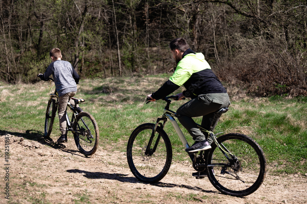 A picturesque scene of two people mountain biking on a trail. Sunlight streams through the trees, creating a bright and vibrant atmosphere. The trail is slightly uneven. A picturesque scene of two people mountain biking on a trail. Sunlight streams through the trees, creating a bright and vibrant atmosphere. The trail is slightly uneven.