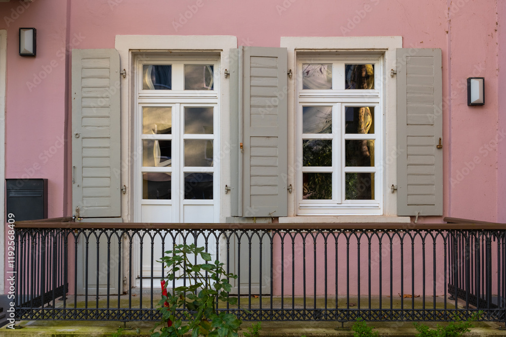 Fototapeta premium Charming pink house with vintage windows and wooden balcony in a quiet neighborhood