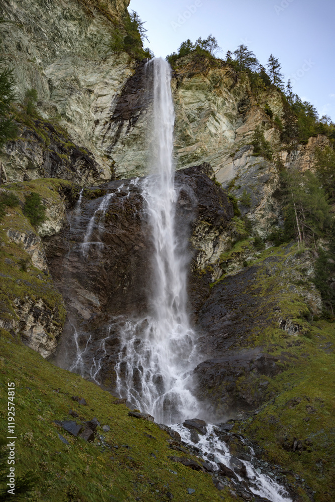 Obraz premium Majestic waterfall cascading down rocky cliffs along the Grossglockner Hochalpenstrasse in Austria during a tranquil afternoon