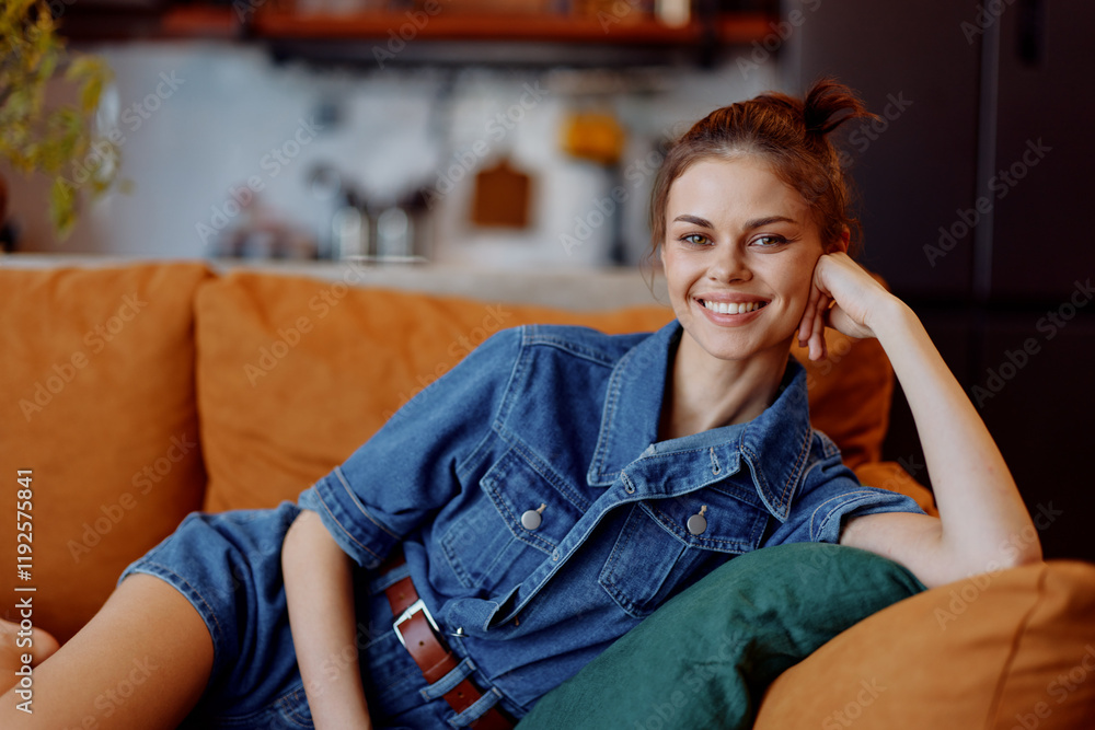 Obraz premium Happy young woman in casual denim shirt relaxing on sofa in cozy living room at home