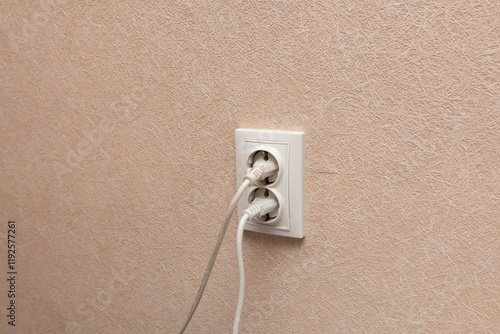 Fotografi Double electrical outlet with two plugs inserted into a beige textured wall