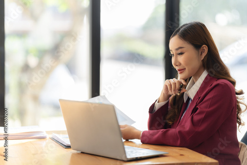 Smiling Asian accountant working with calculator and analyzing financial documents on laptop at table surrounded by documents on table Free Download Smiling Asian accountant working with calculator and analyzing financial documents on laptop at table surrounded by documents on table - GFXLoad