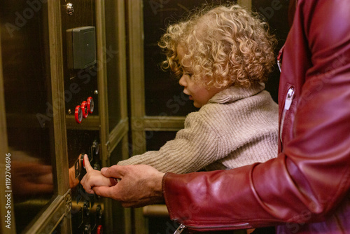 Curly-haired child learning to press an elevator button with the help of an adult's guiding hand. Cleveland Public Library, Ohio, USA photo