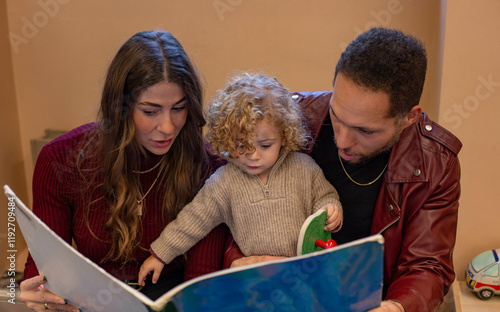 Parents and their young child are engaged in reading a large picture book together, with focus and enjoyment evident in their interaction. Cleveland, Ohio, USA photo