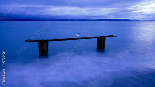 A serene seascape at dusk features a blue-tinted sky and calm ocean, with an old wooden beam supporting a crystal ball, Norwegian Point, WA, USA photo