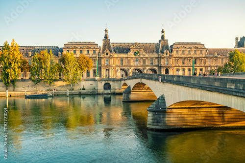 Elegant historical building of the Louvre Museum and bridge over a calm Seine river at sunset, with clear skies and warm sunlight bathing the scene, Paris, France photo