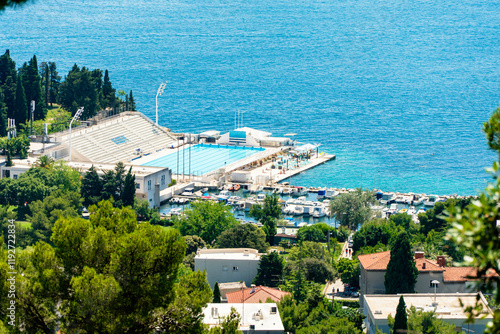 Aerial view of an outdoor olympic swimming pool, boats docked in a small marina, surrounded by lush greenery in Split, Croatia photo