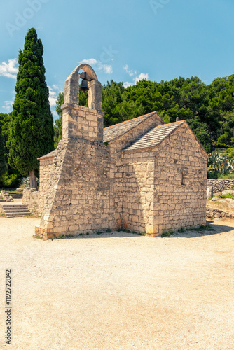 Old stone church of St. Nicholas with a bell tower under clear blue sky, surrounded by Mediterranean foliage, Split, Croatia photo