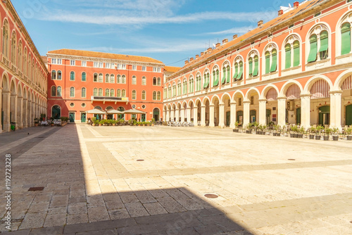 A spacious courtyard at the Republic Square surrounded by classical arcades with vibrant green and red facades under a clear blue sky, Split, Croatia photo