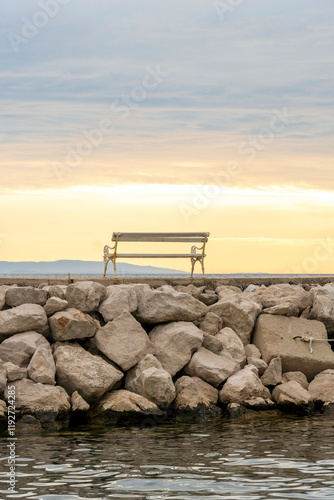 A solitary bench perched on a rocky breakwater under a serene sky at sunset, Podgora, Croatia photo