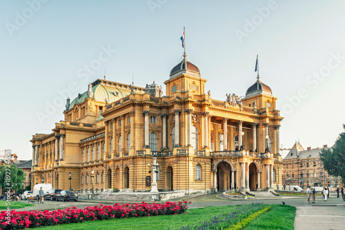 Golden hour sunlight bathes the elegant historic theater opera house of Zagreb with people milling around its entrance amidst vibrant city life, Zagreb, Croatia photo