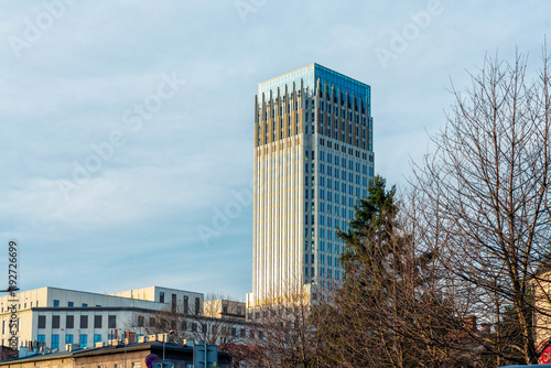 Modern skyscraper gleaming in the sunset light by Rondo Mogilskie against a clear blue sky with trees in the foreground, Krakow, Poland