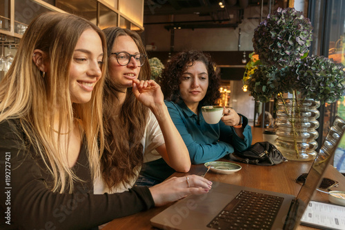 Three women engaging in conversation at a cafe table while one operates a laptop, Berlin, Germany photo