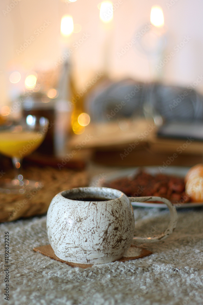Fototapeta premium Books, e-reader, tea, orange juice, fruit, snacks, yarn, blanket and lit candles on the table. Autumn or winter at home. Selective focus.