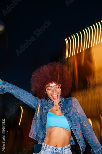 Joyful African descendant woman with afro hair dancing at night